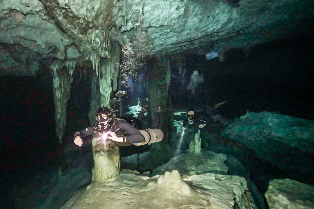 Two scuba divers in sidemount gear in a submerged cavern in Mexico