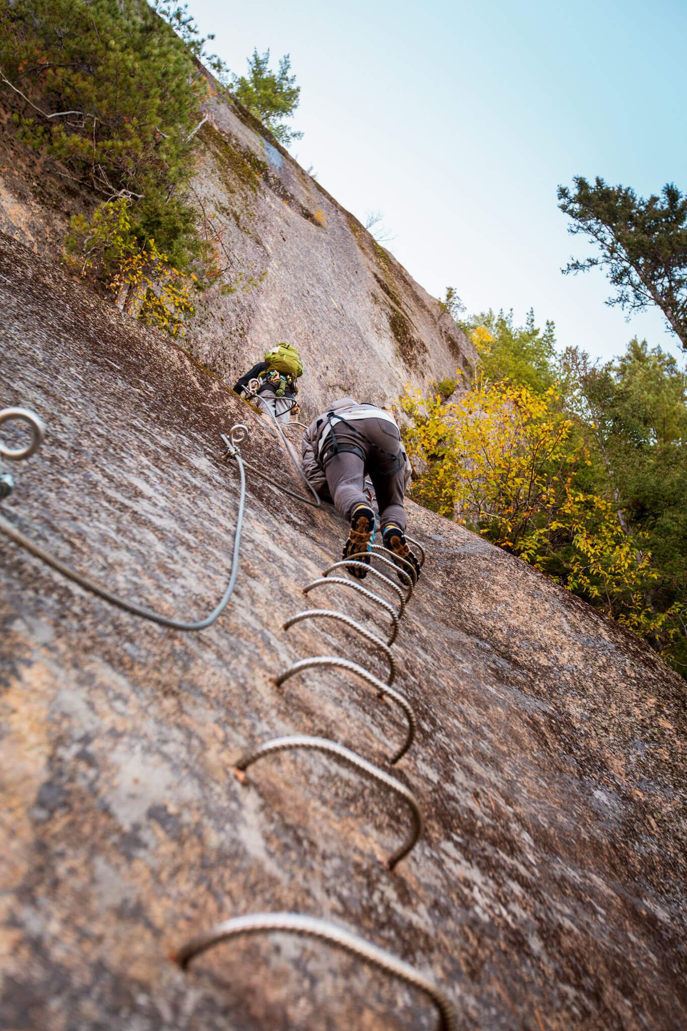 Rock climbers ascend a sheer cliff on a via ferrata route in the Saguenay Fjord National Park