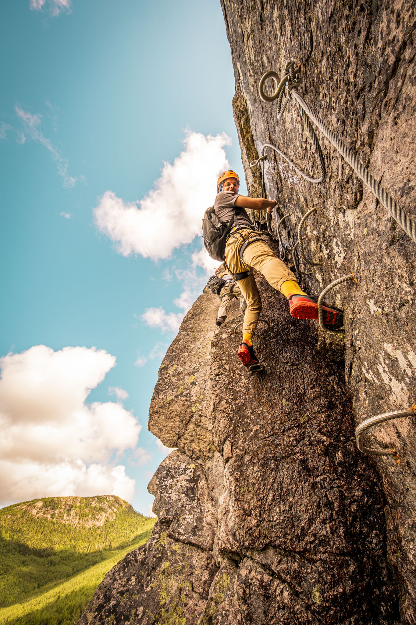 Via ferrata climber ascends vertical rock cliff at Parc national des Grands-Jardins