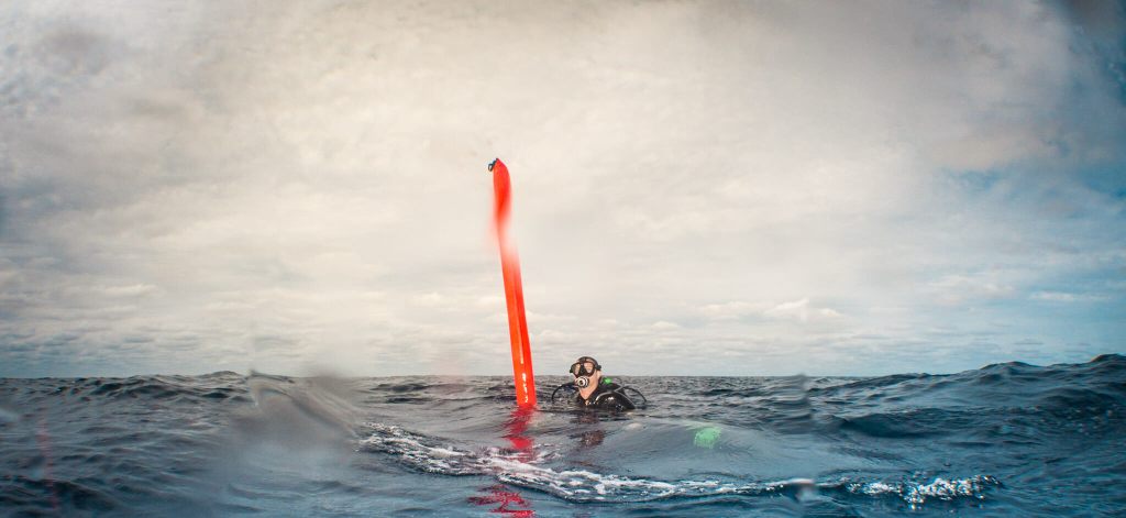 Scuba diver at the surface with a deployed delayed surface marker buoy (DSMB)