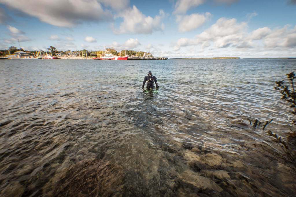 A scuba diver in a drysuit enters the water at The Tugs dive site in Tobermory