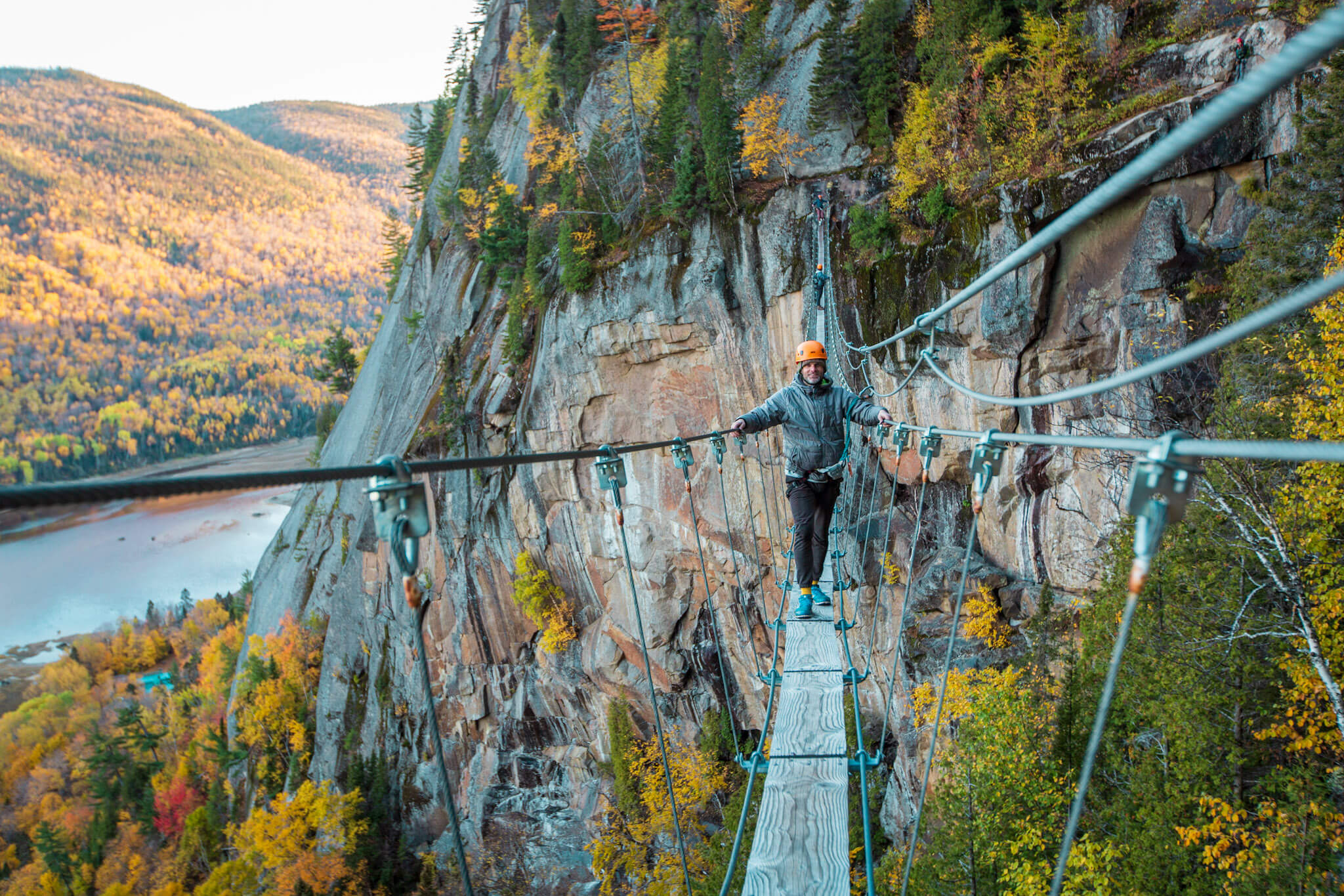 A climber poses for a photo on a narrow foot bridge suspended between two rock cliffs